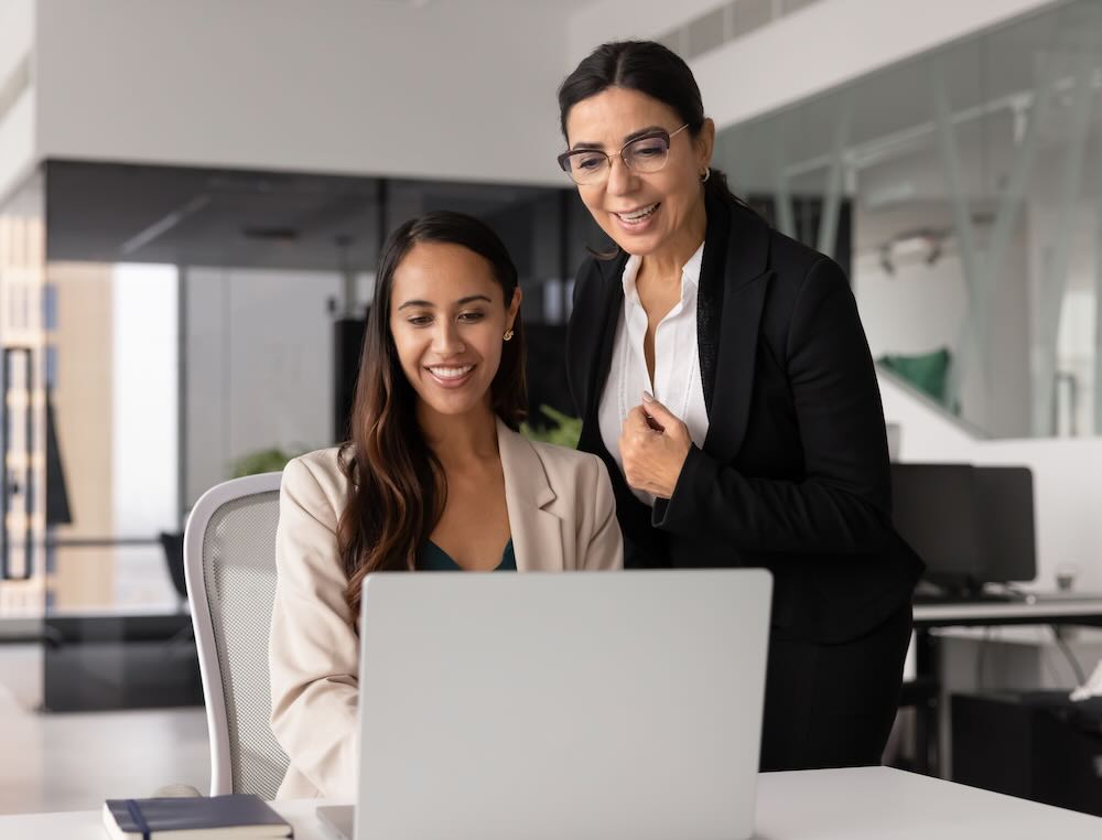 Two female coworkers engage in productive teamwork using laptop in modern office